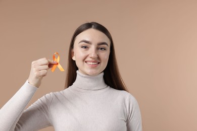 Photo of Multiple Sclerosis awareness. Happy young woman holding orange ribbon on beige background