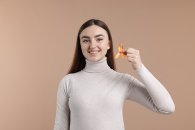 Photo of Multiple Sclerosis awareness. Happy young woman holding orange ribbon on beige background