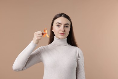 Photo of Multiple Sclerosis awareness. Young woman holding orange ribbon on beige background