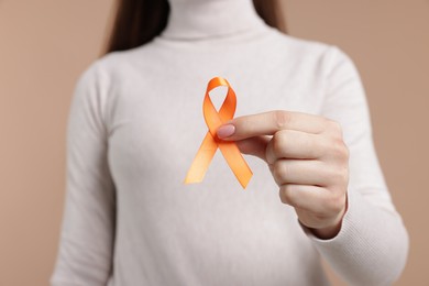 Photo of Multiple Sclerosis awareness. Young woman holding orange ribbon on beige background, closeup