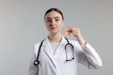 Photo of Multiple Sclerosis awareness. Doctor holding orange ribbon on light grey background