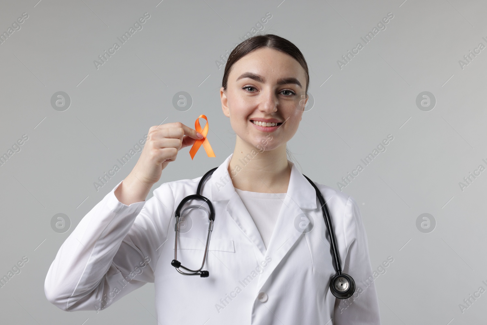 Photo of Multiple Sclerosis awareness. Happy doctor holding orange ribbon on light grey background