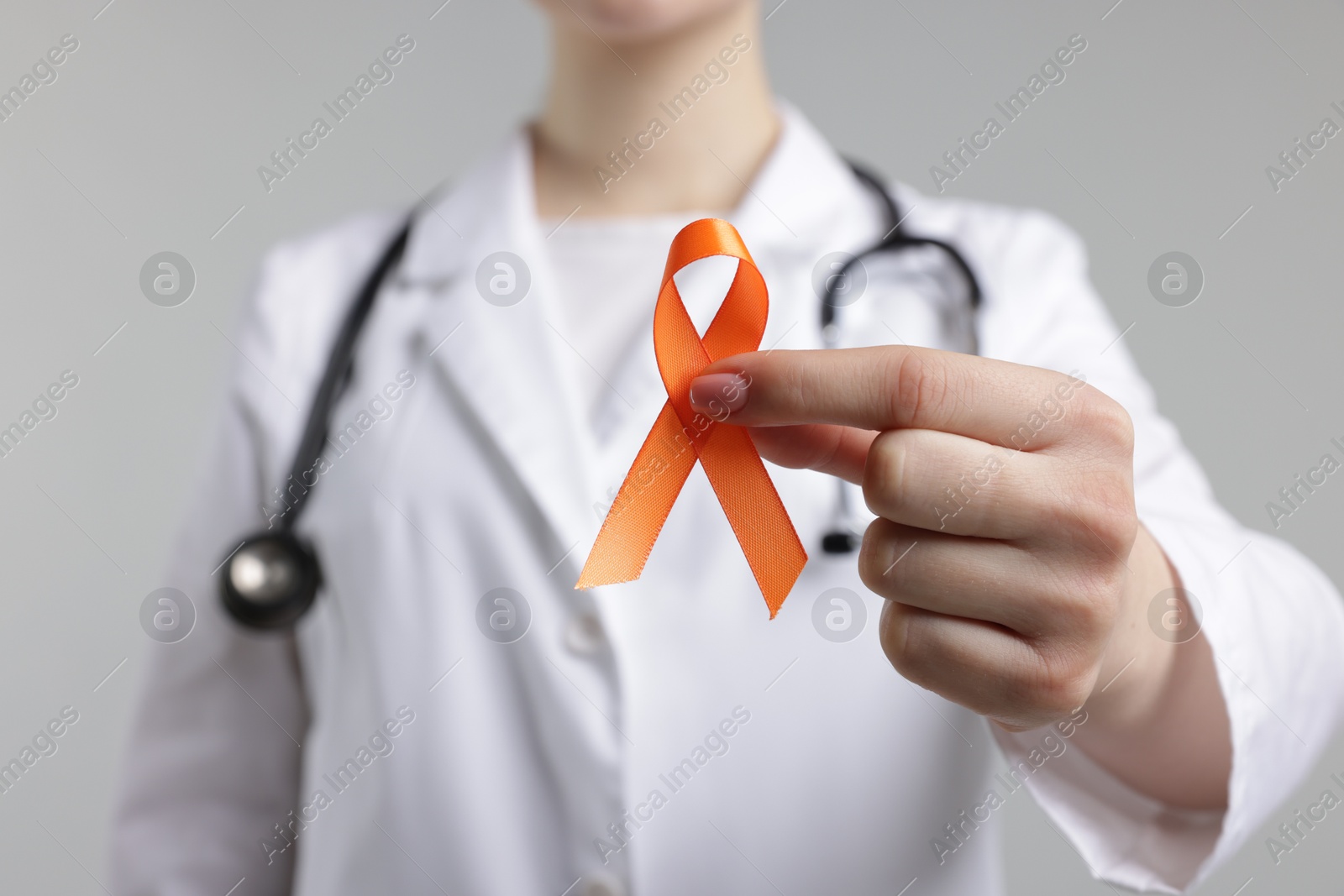 Photo of Multiple Sclerosis awareness. Doctor holding orange ribbon on light grey background, closeup