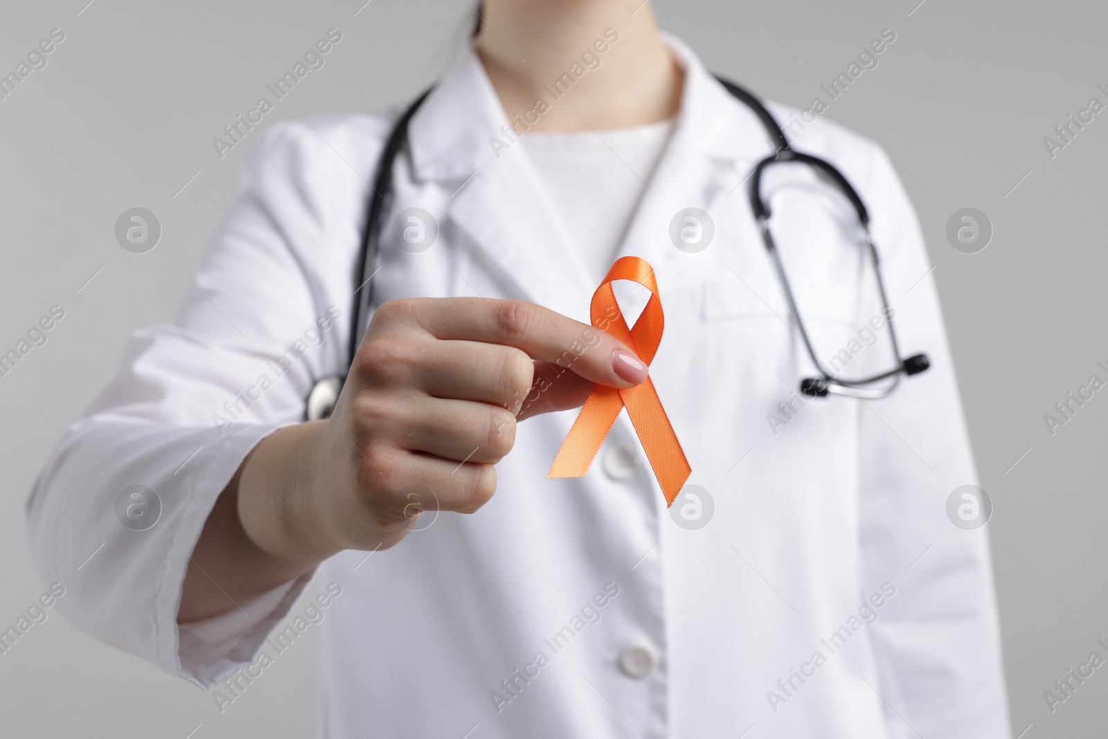 Photo of Multiple Sclerosis awareness. Doctor holding orange ribbon on light grey background, closeup