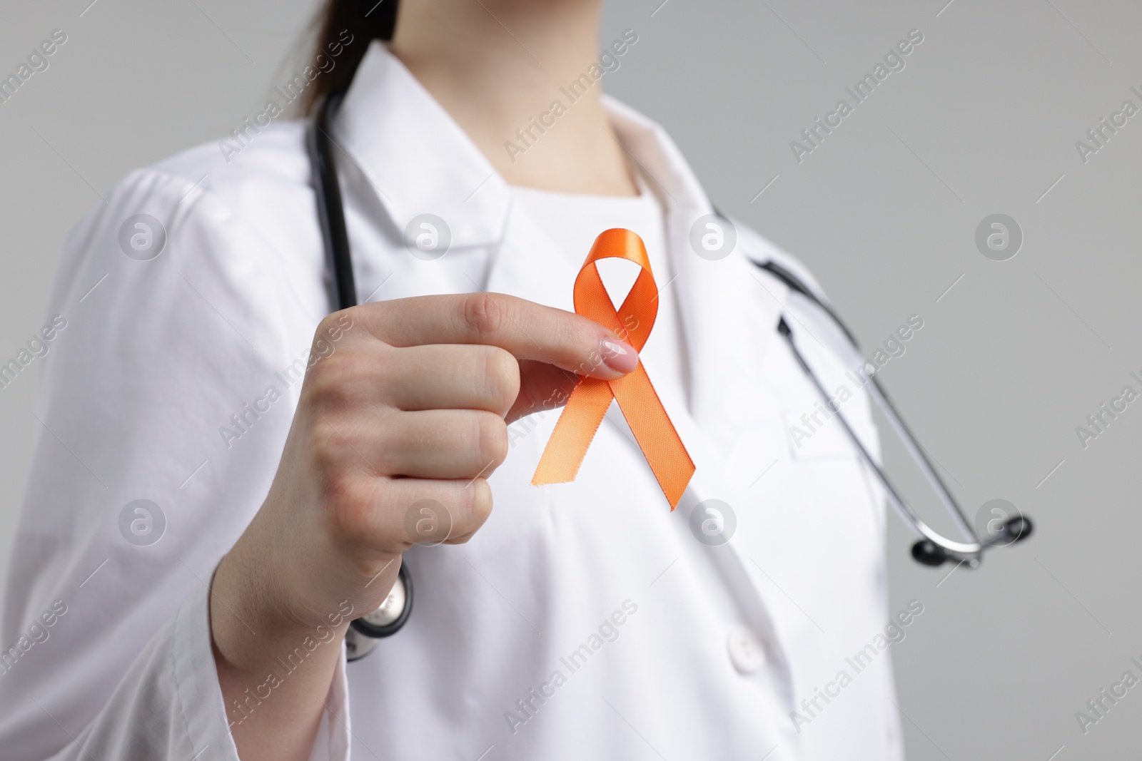 Photo of Multiple Sclerosis awareness. Doctor holding orange ribbon on light grey background, closeup