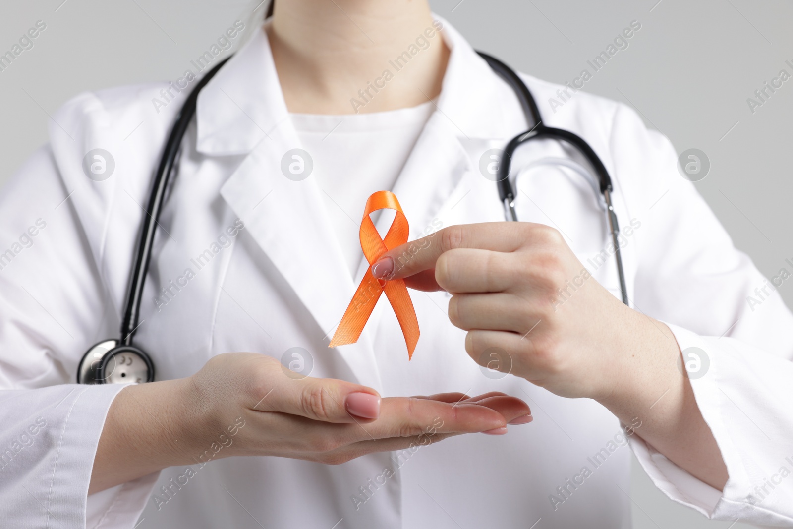 Photo of Multiple Sclerosis awareness. Doctor holding orange ribbon on light grey background, closeup