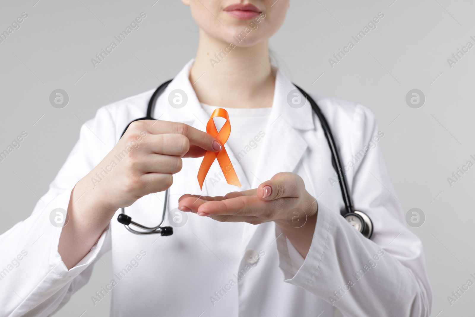 Photo of Multiple Sclerosis awareness. Doctor holding orange ribbon on light grey background, closeup