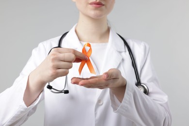 Photo of Multiple Sclerosis awareness. Doctor holding orange ribbon on light grey background, closeup