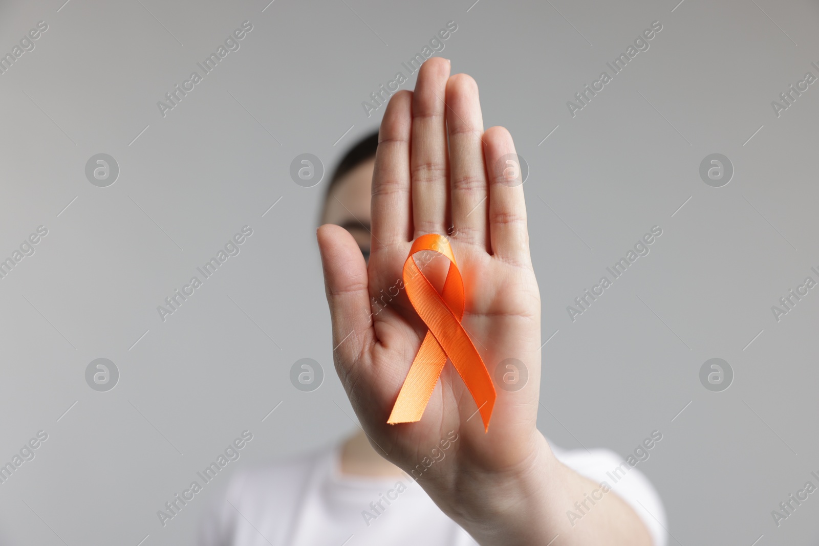 Photo of Multiple Sclerosis awareness. Young woman holding orange ribbon on light grey background, selective focus