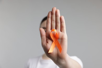 Photo of Multiple Sclerosis awareness. Young woman holding orange ribbon on light grey background, selective focus