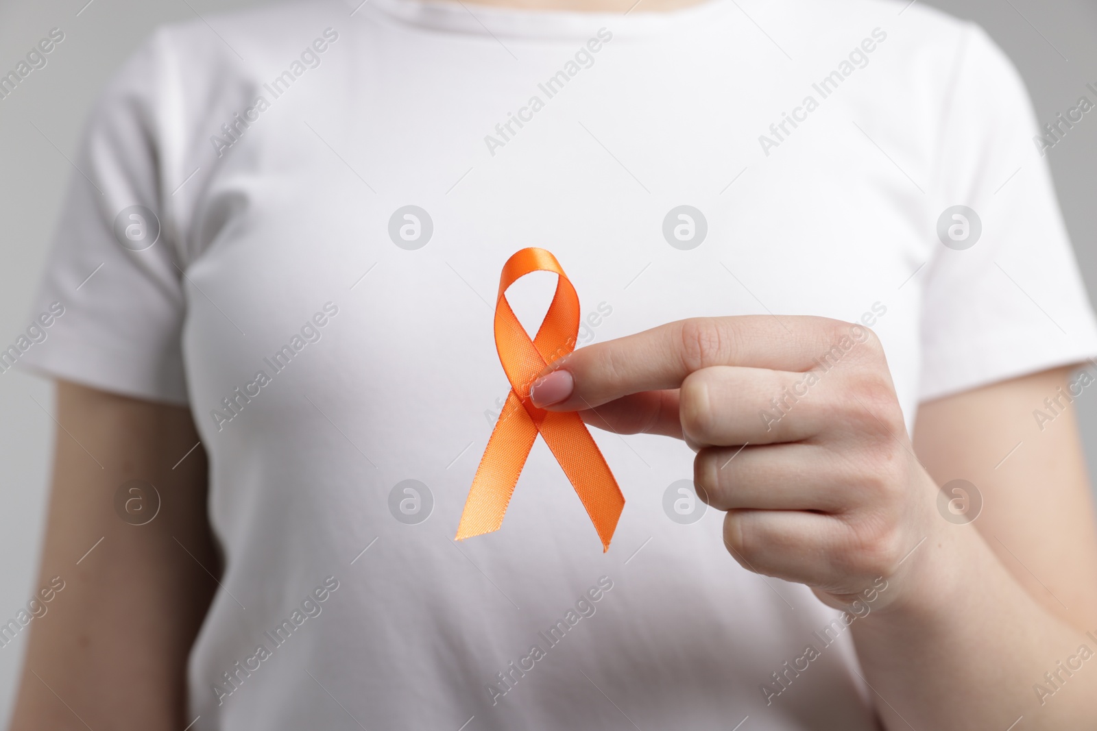 Photo of Multiple Sclerosis awareness. Young woman holding orange ribbon on light grey background, closeup