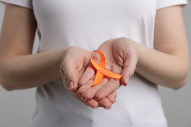 Photo of Multiple Sclerosis awareness. Young woman holding orange ribbon on light grey background, closeup