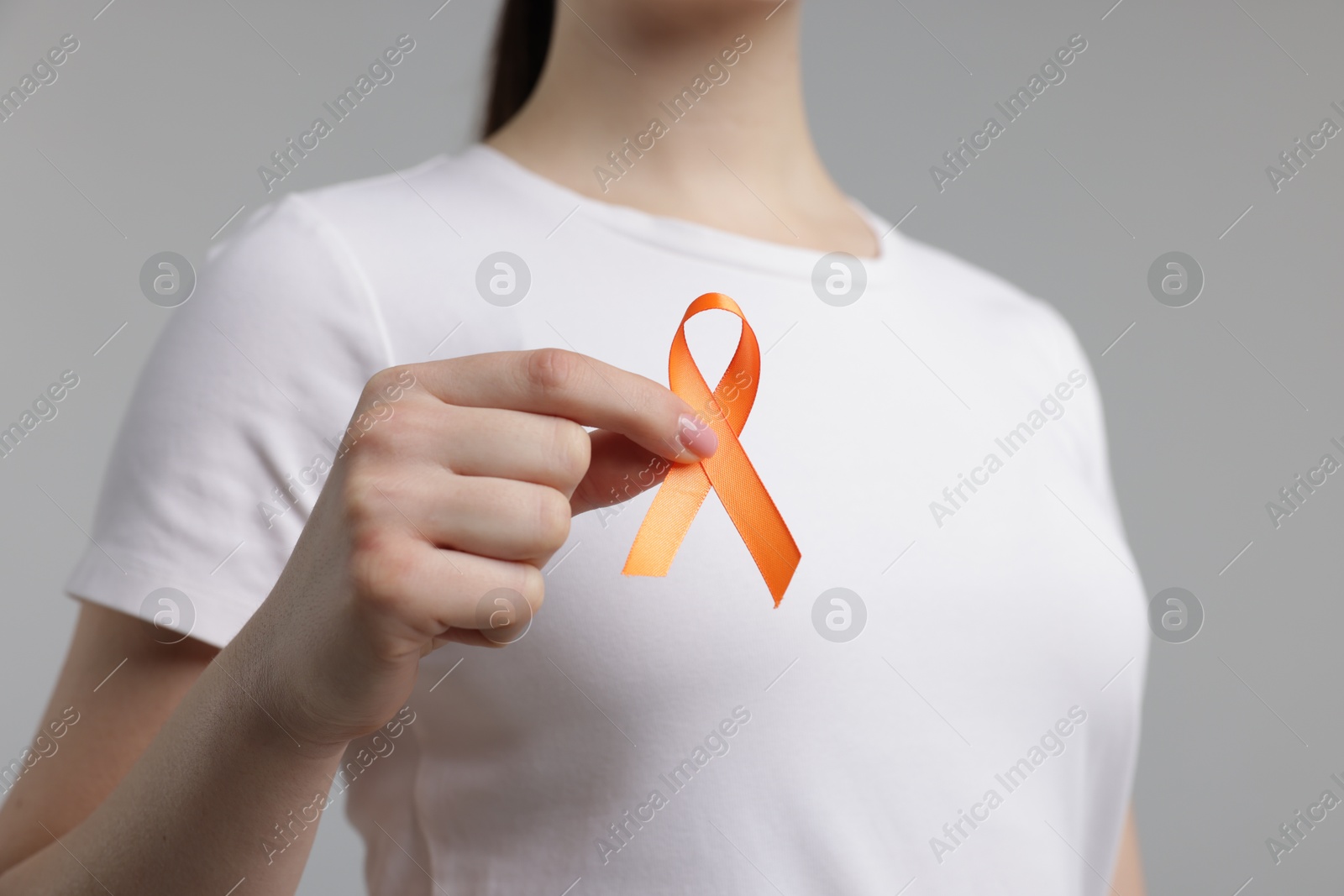 Photo of Multiple Sclerosis awareness. Young woman holding orange ribbon on light grey background, closeup