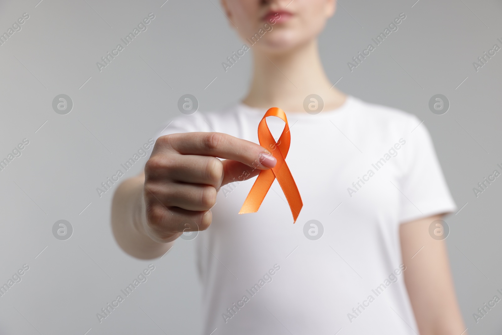 Photo of Multiple Sclerosis awareness. Young woman holding orange ribbon on light grey background, closeup