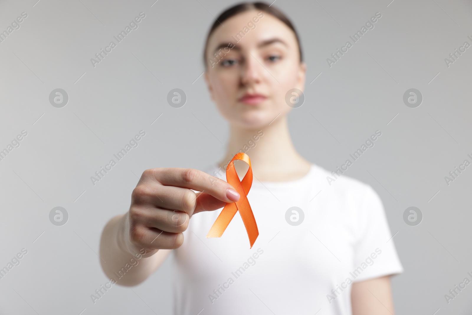 Photo of Multiple Sclerosis awareness. Young woman holding orange ribbon on light grey background, selective focus