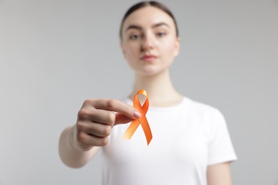 Photo of Multiple Sclerosis awareness. Young woman holding orange ribbon on light grey background, selective focus