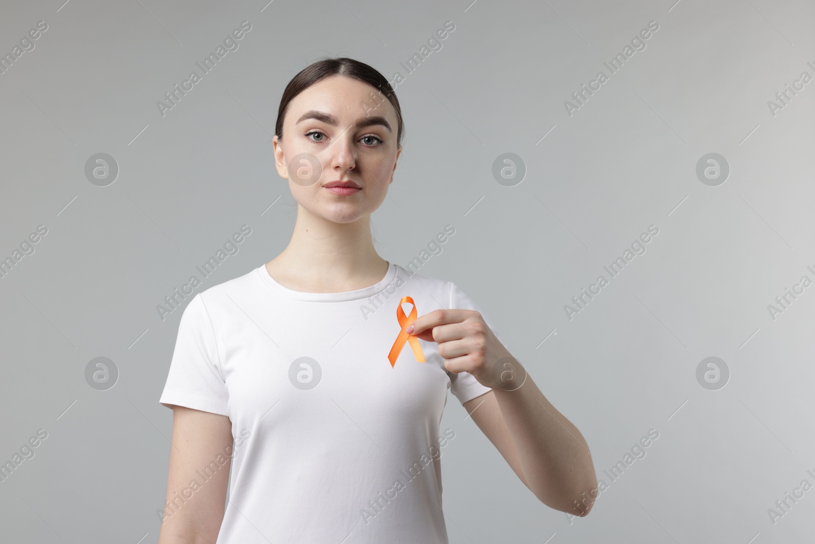 Photo of Multiple Sclerosis awareness. Young woman holding orange ribbon on light grey background