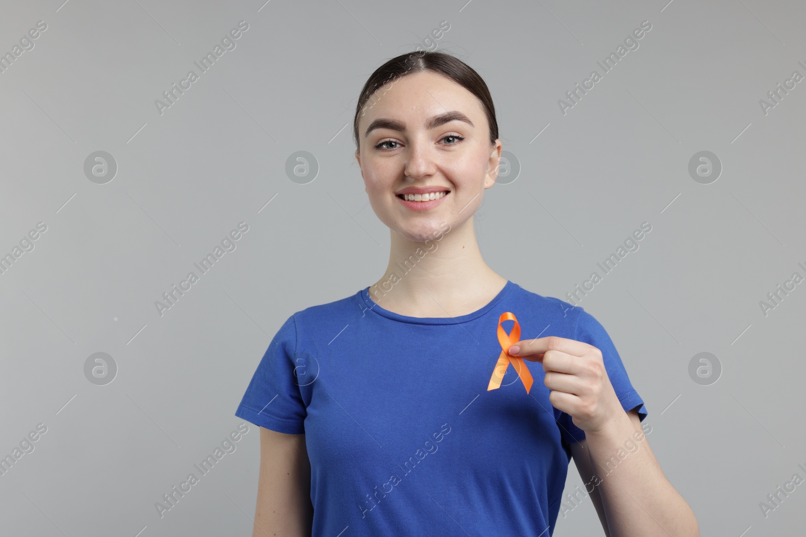 Photo of Multiple Sclerosis awareness. Happy young woman holding orange ribbon on light grey background