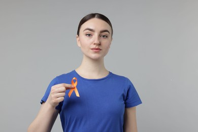 Photo of Multiple Sclerosis awareness. Young woman holding orange ribbon on light grey background