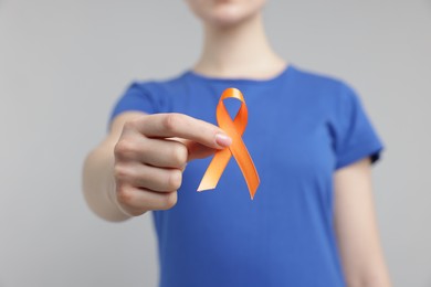 Photo of Multiple Sclerosis awareness. Young woman holding orange ribbon on light grey background, closeup