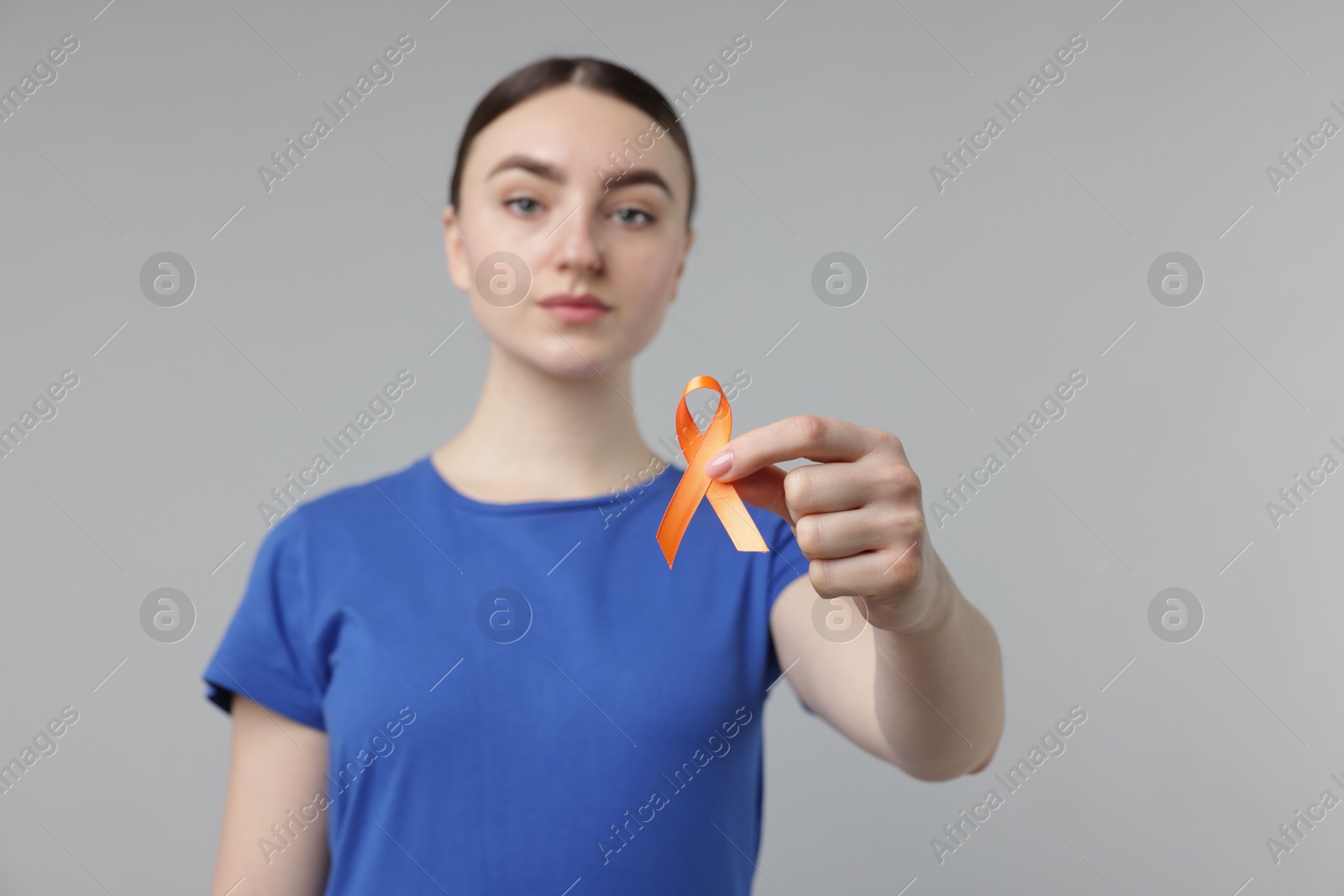 Photo of Multiple Sclerosis awareness. Young woman holding orange ribbon on light grey background, selective focus