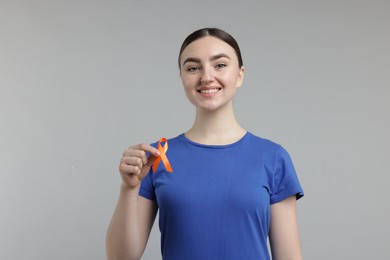 Photo of Multiple Sclerosis awareness. Happy young woman holding orange ribbon on light grey background