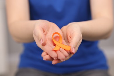 Photo of Multiple Sclerosis awareness. Young woman holding orange ribbon on blurred background, closeup