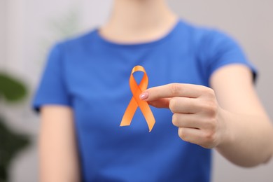 Photo of Multiple Sclerosis awareness. Young woman holding orange ribbon indoors, closeup