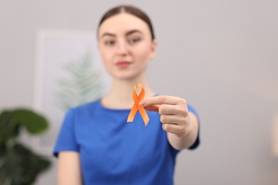 Photo of Multiple Sclerosis awareness. Young woman holding orange ribbon indoors, selective focus