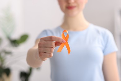 Photo of Multiple Sclerosis awareness. Young woman holding orange ribbon indoors, closeup