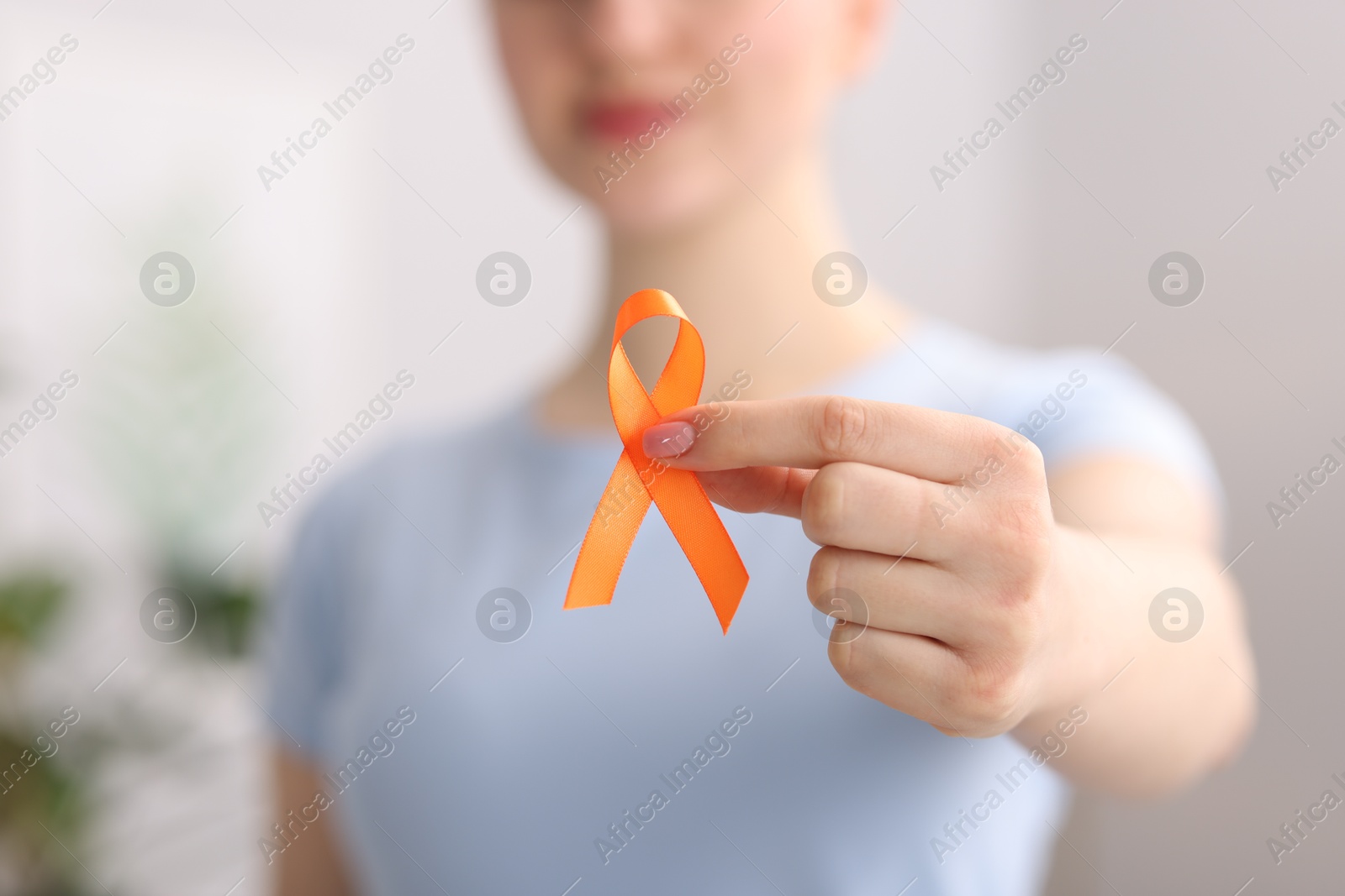 Photo of Multiple Sclerosis awareness. Young woman holding orange ribbon indoors, closeup