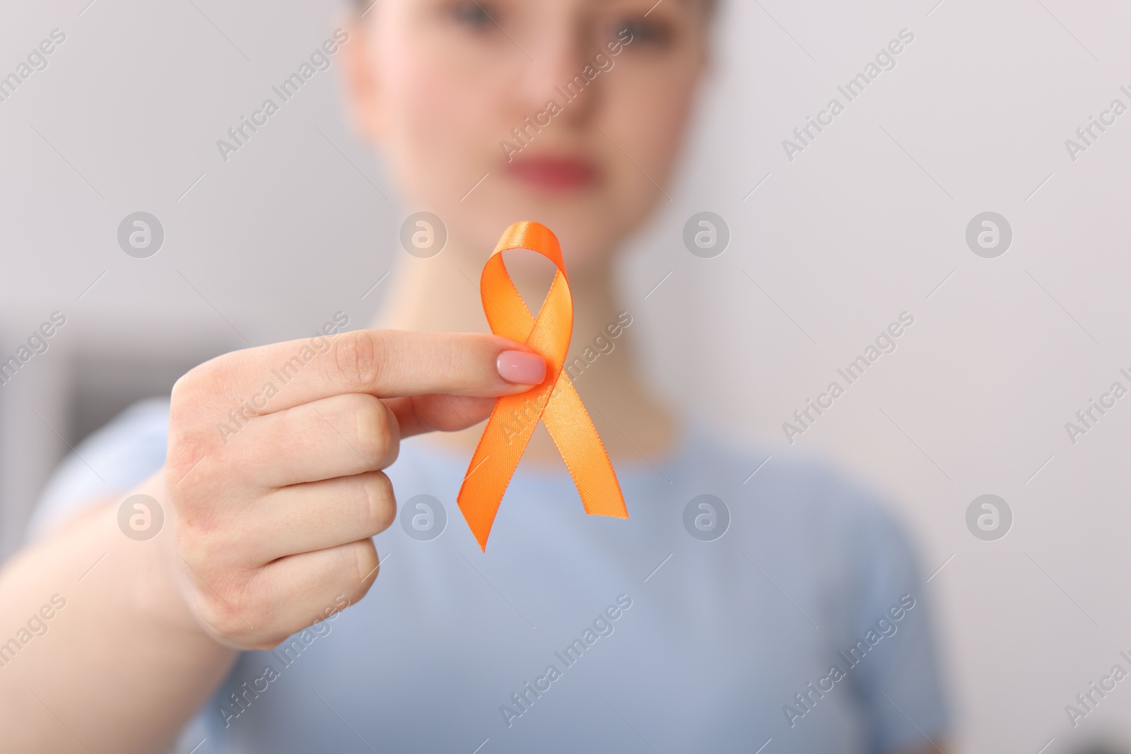 Photo of Multiple Sclerosis awareness. Young woman holding orange ribbon indoors, selective focus