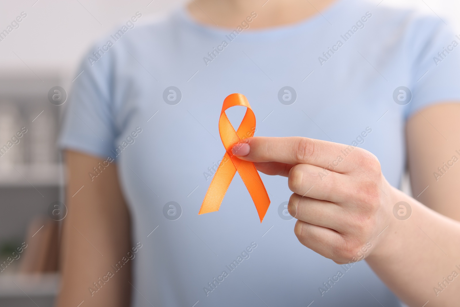 Photo of Multiple Sclerosis awareness. Young woman holding orange ribbon indoors, closeup