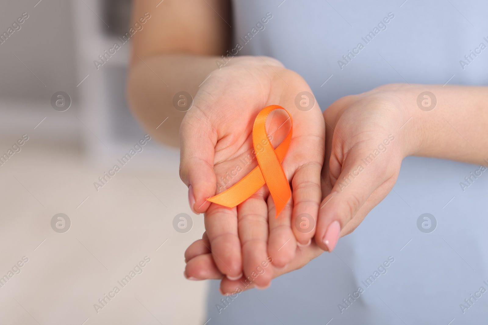 Photo of Multiple Sclerosis awareness. Young woman holding orange ribbon indoors, closeup