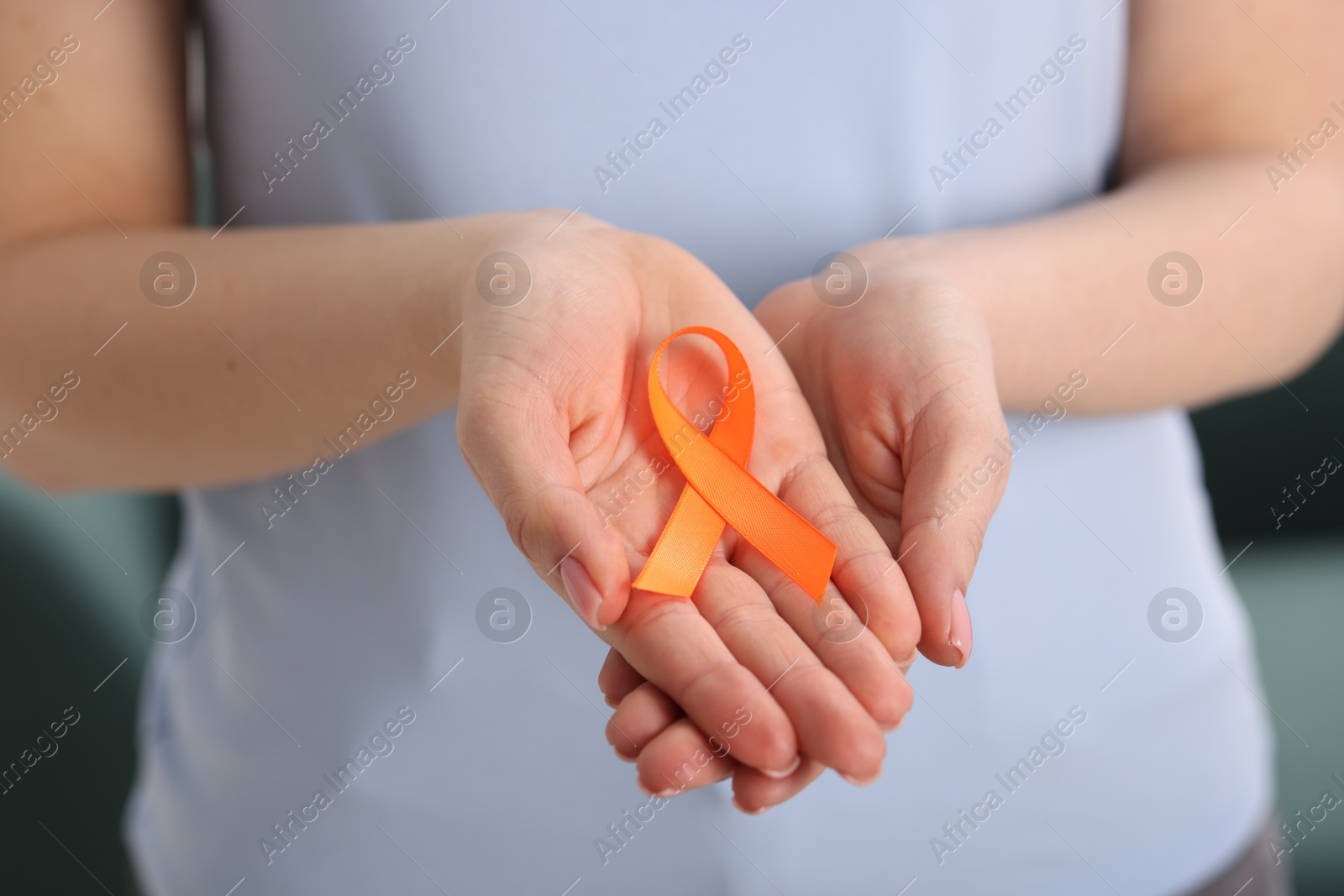 Photo of Multiple Sclerosis awareness. Young woman holding orange ribbon indoors, closeup