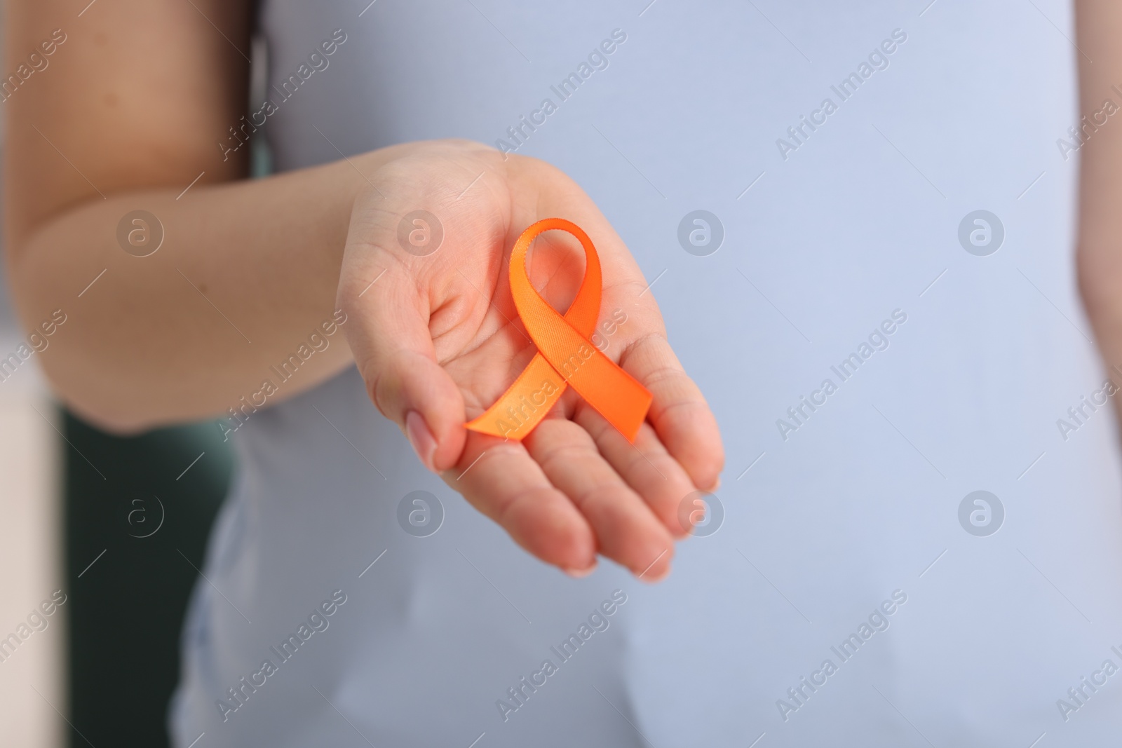 Photo of Multiple Sclerosis awareness. Young woman holding orange ribbon indoors, closeup