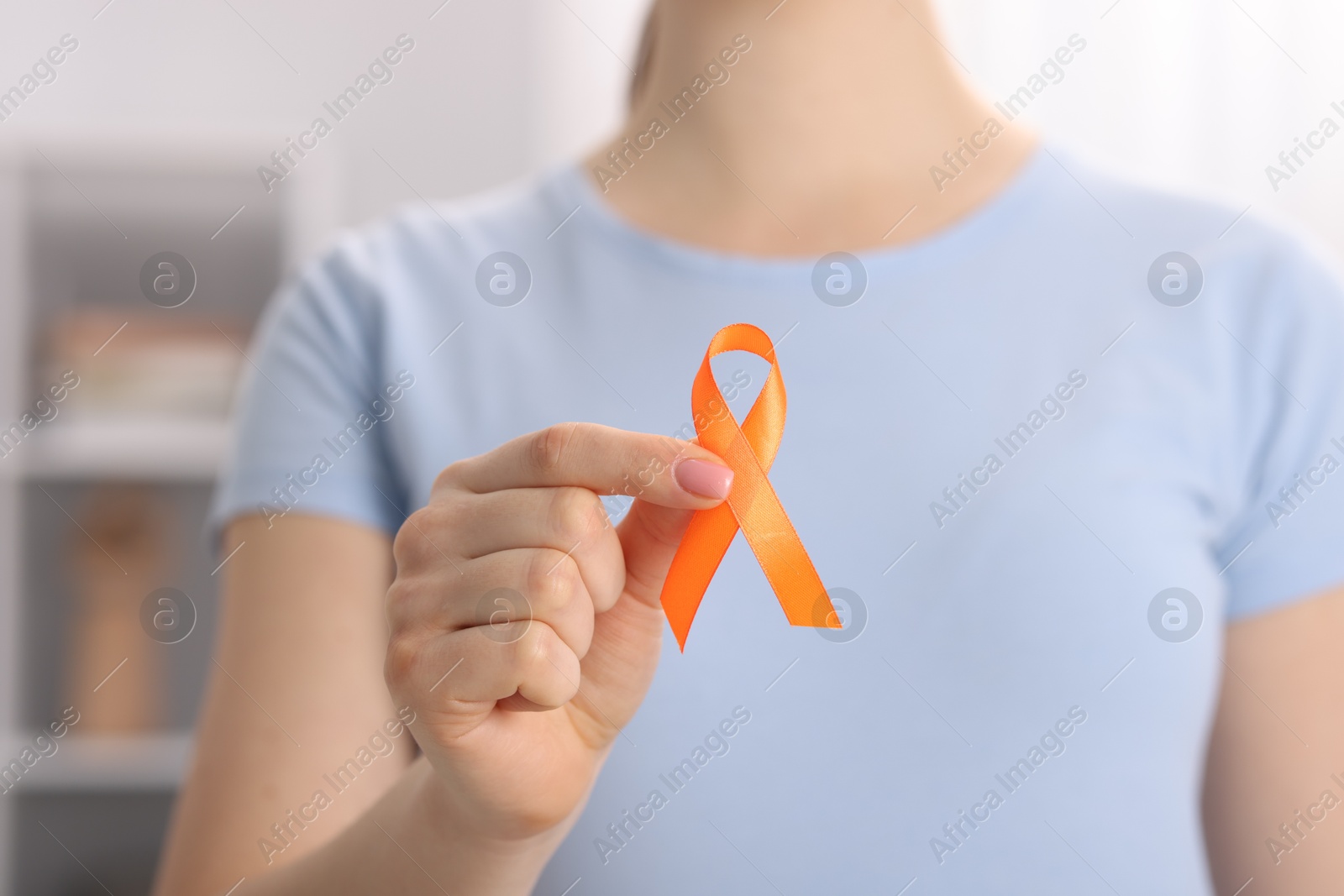 Photo of Multiple Sclerosis awareness. Young woman holding orange ribbon indoors, closeup