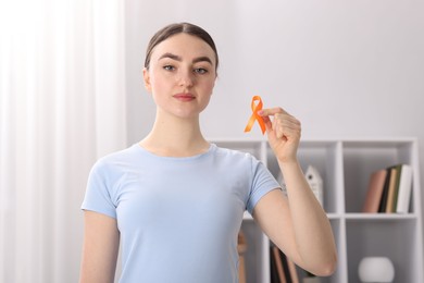 Photo of Multiple Sclerosis awareness. Young woman holding orange ribbon indoors