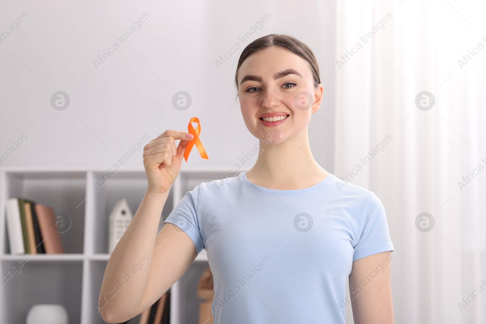 Photo of Multiple Sclerosis awareness. Happy young woman holding orange ribbon indoors