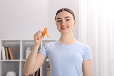 Photo of Multiple Sclerosis awareness. Happy young woman holding orange ribbon indoors