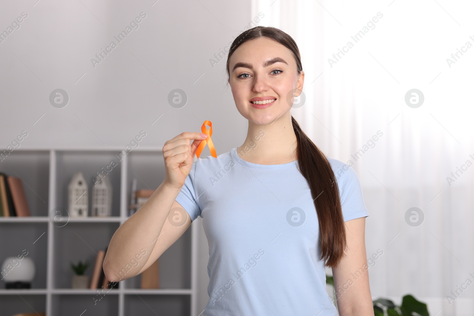 Photo of Multiple Sclerosis awareness. Happy young woman holding orange ribbon indoors