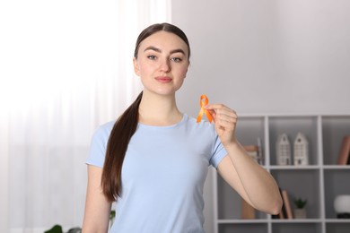 Photo of Multiple Sclerosis awareness. Young woman holding orange ribbon indoors