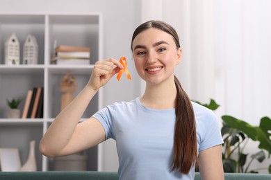 Photo of Multiple Sclerosis awareness. Happy young woman holding orange ribbon indoors