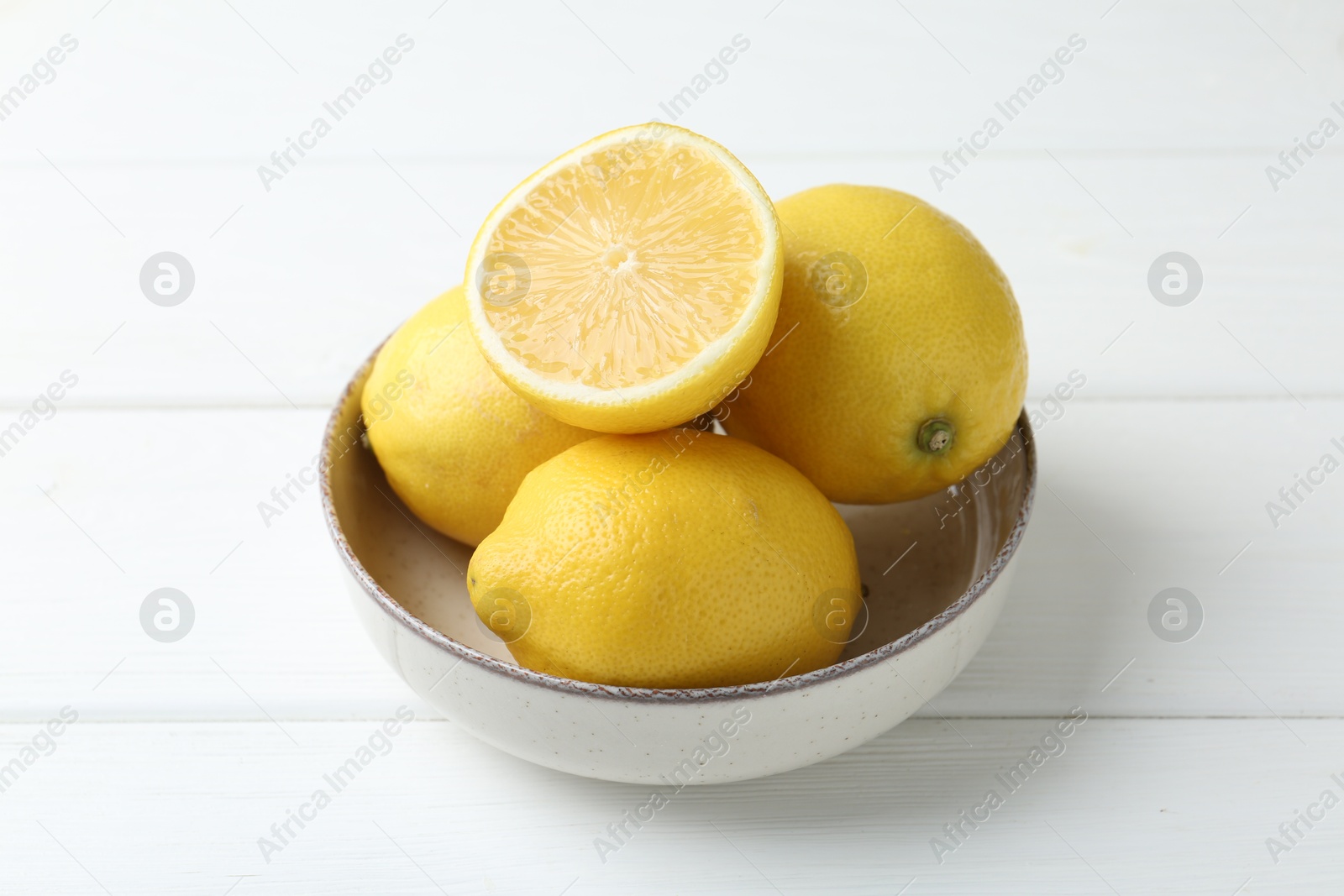 Photo of Fresh whole and cut lemons in bowl on white wooden table, closeup