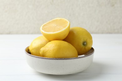 Photo of Fresh whole and cut lemons in bowl on white wooden table, closeup