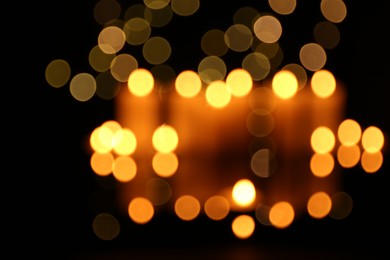 Photo of Blurred view of burning candles in darkness, bokeh effect