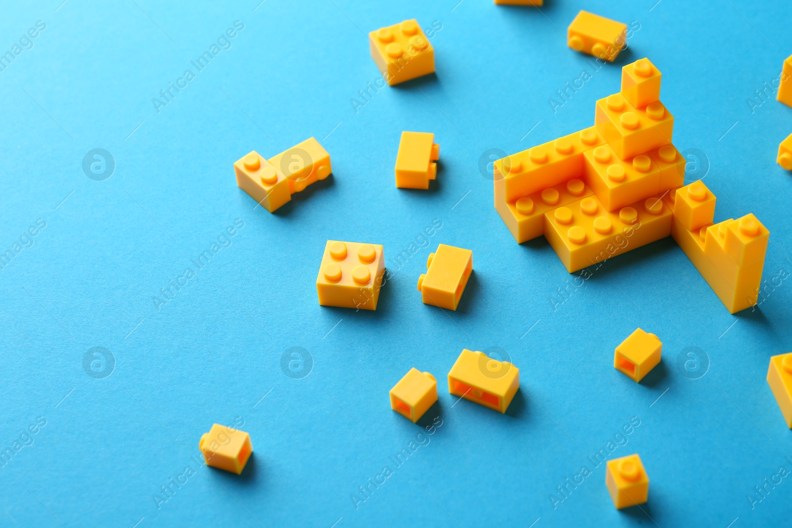 Photo of Constructor toy. Many yellow building blocks on light blue background, space for text