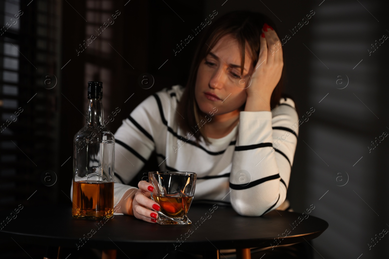 Photo of Alcohol addiction. Woman with glass of whiskey and bottle at table indoors