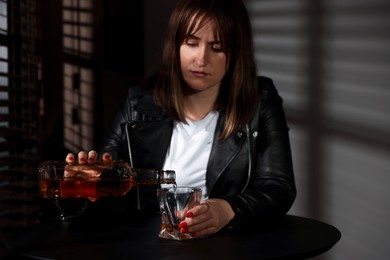 Photo of Alcohol addiction. Woman pouring whiskey into glass at table indoors