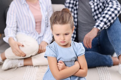 Photo of Resentful little girl and her parents at home. Family dispute